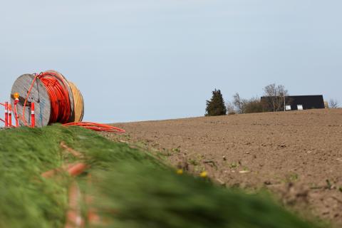 A broadband line lays on grass next to a farm.